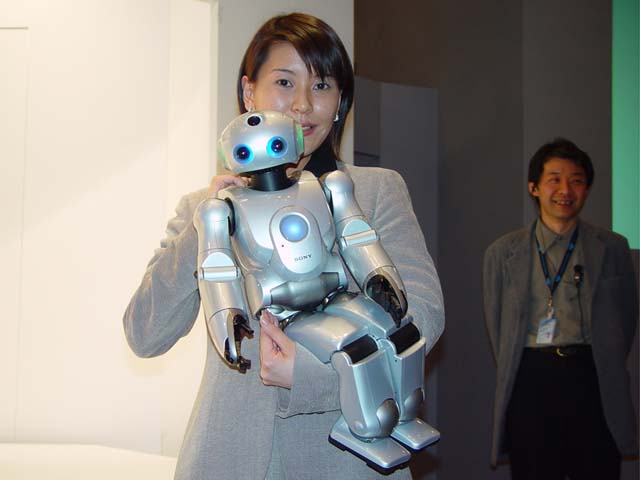 woman holds sony robot in her arms, man looks on